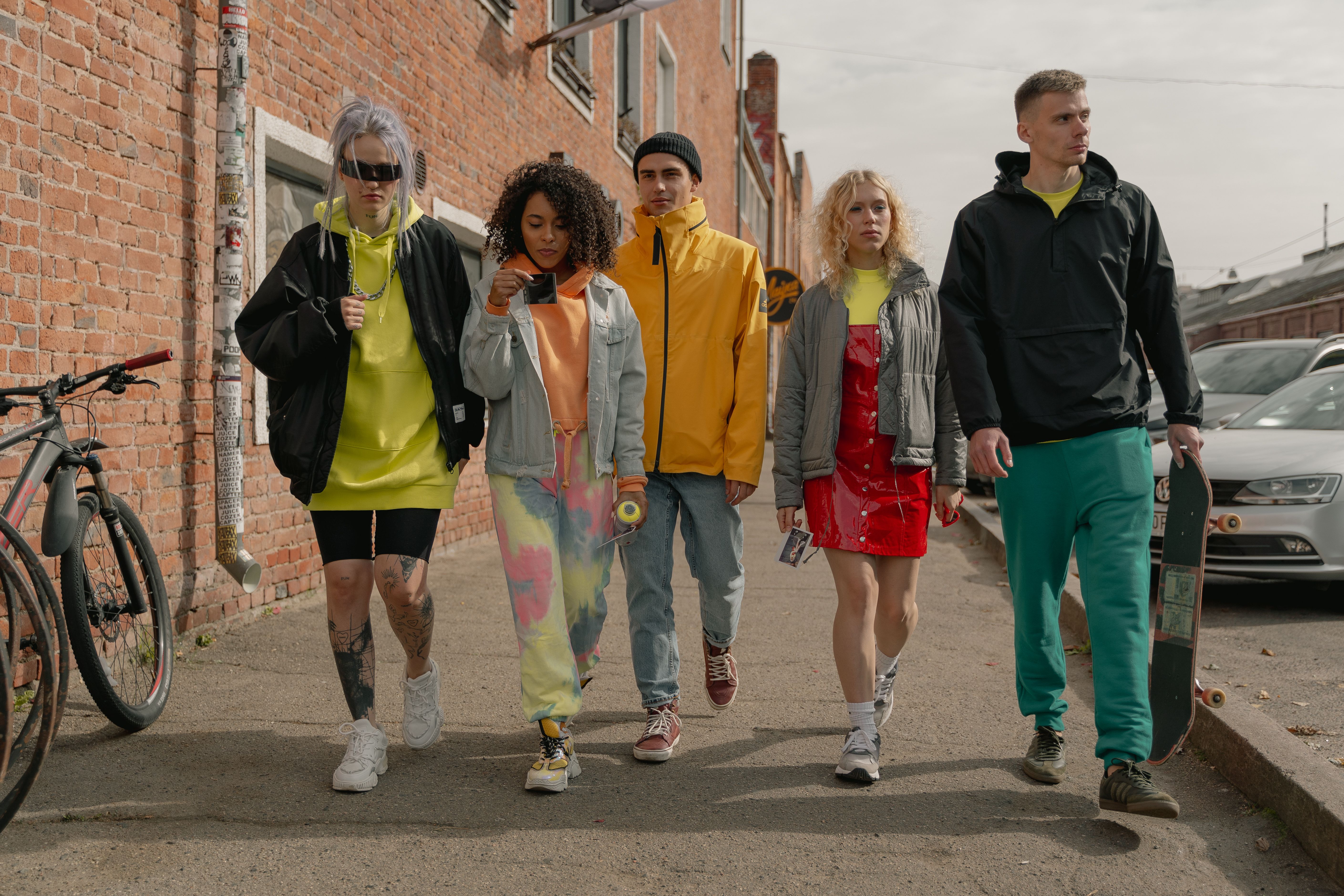 Five friends in colourful graphic streetwear tees walking down a brick-lined street — mcdizains.com printed t-shirts